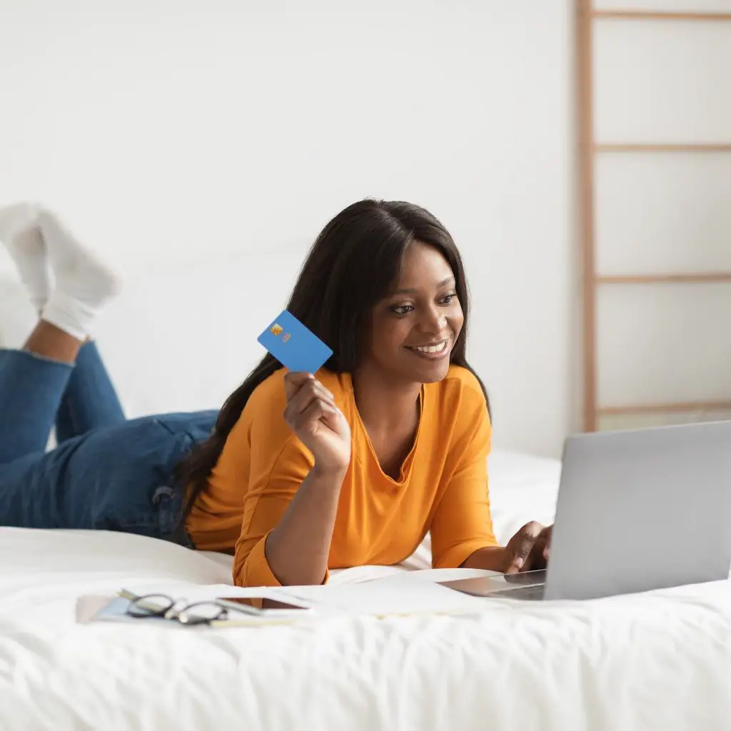 African Woman Shopping Using Laptop And Credit Card In Bedroom