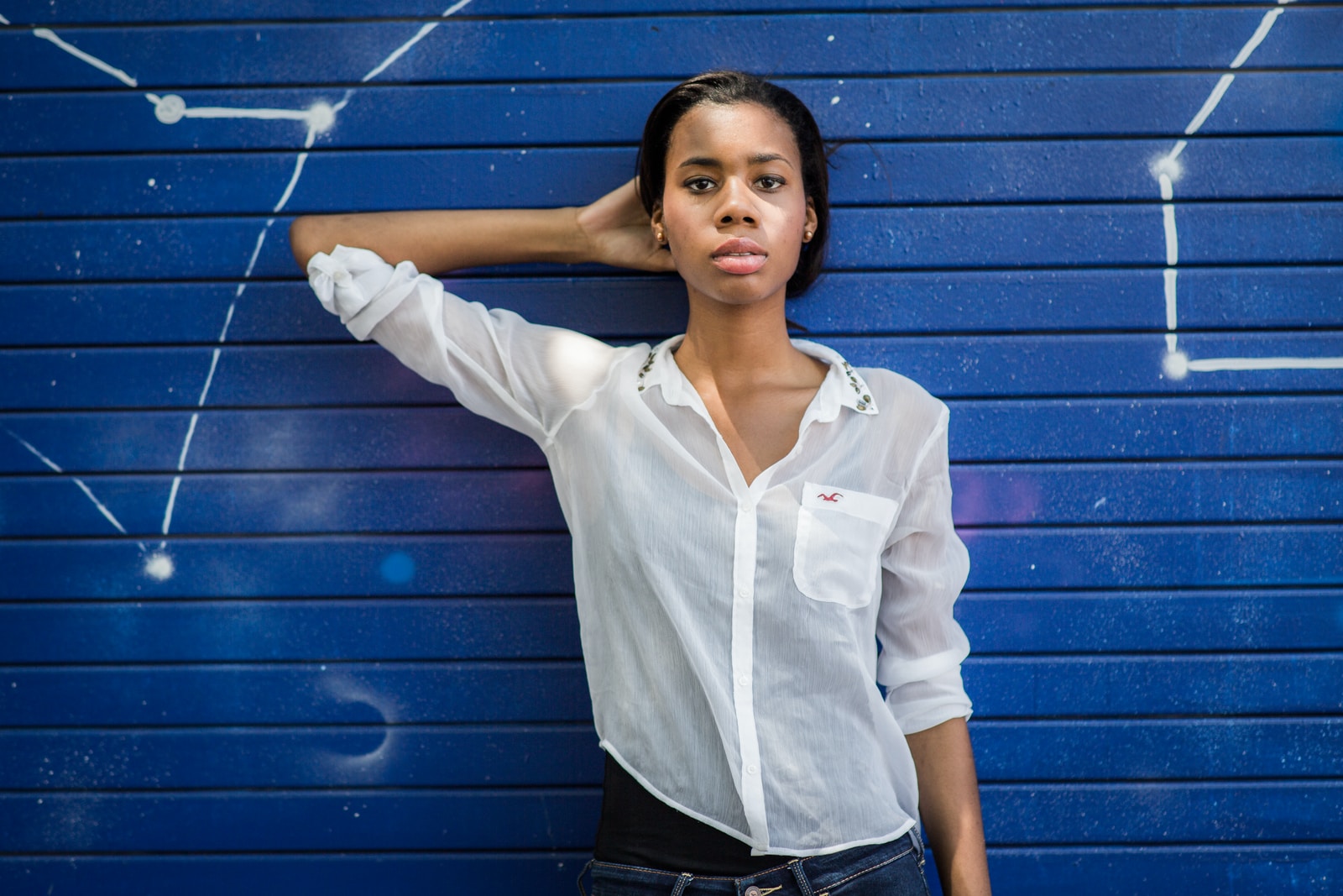 student in white dress shirt and black pants standing beside blue wall