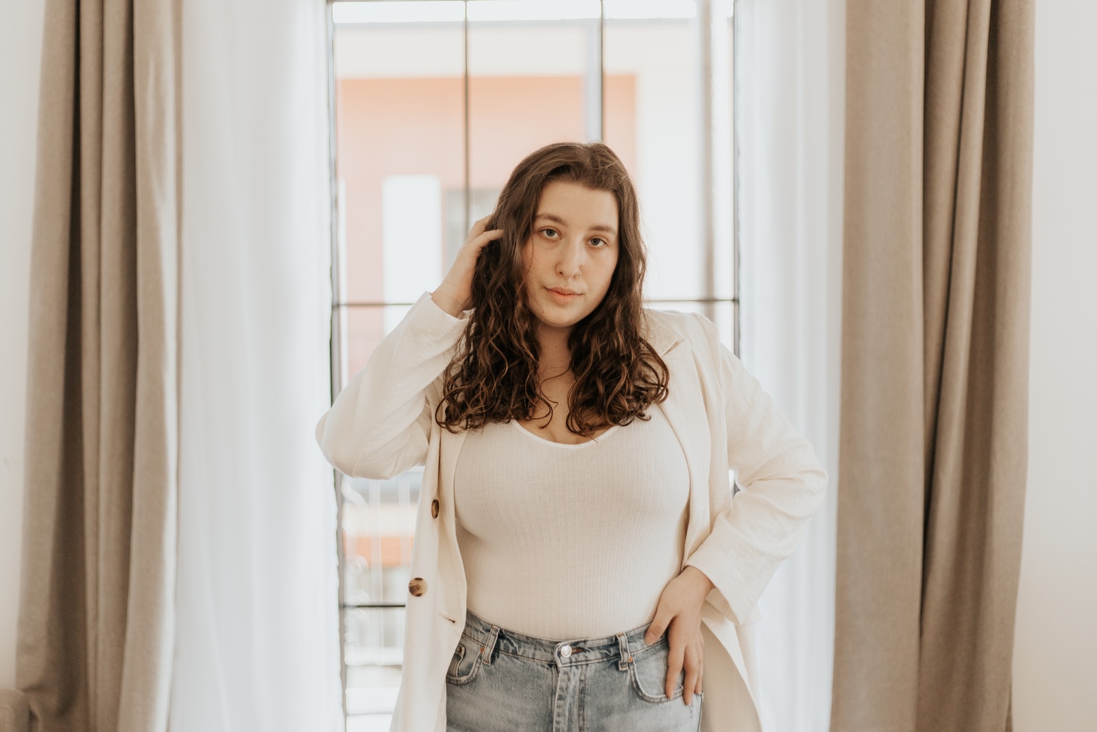 student in white long sleeve crop top and blue denim jeans standing near window