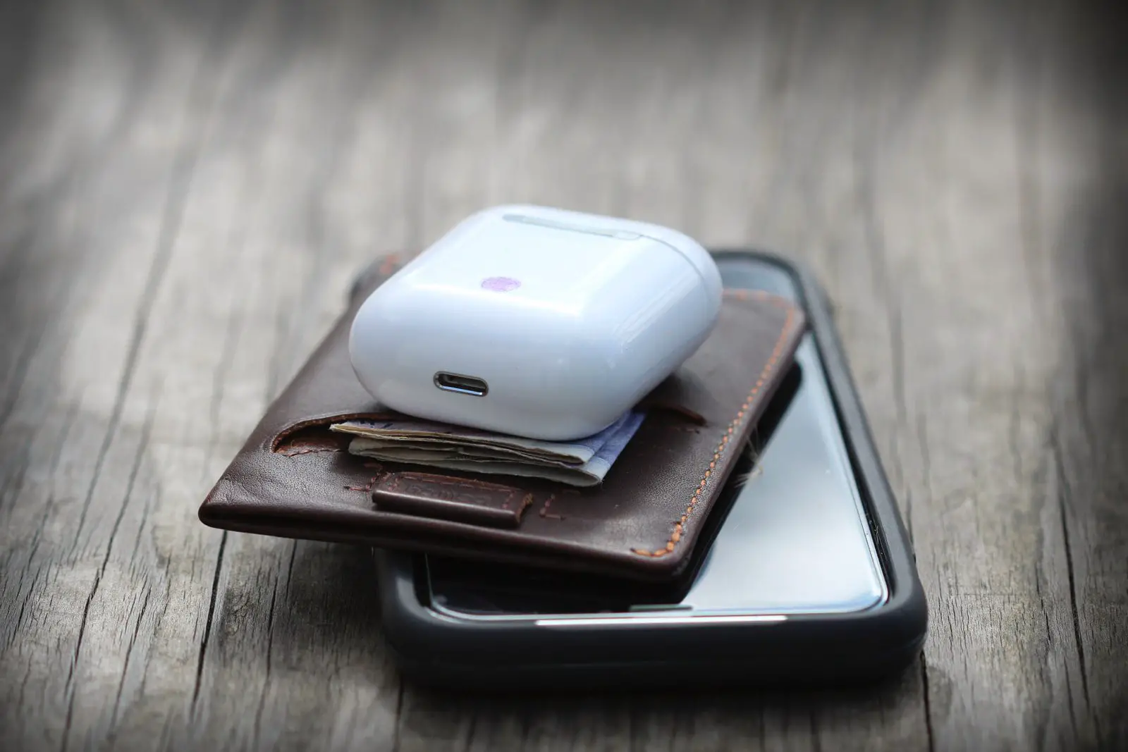 white wireless mini earphones and brown leather wallet on top of otterbox