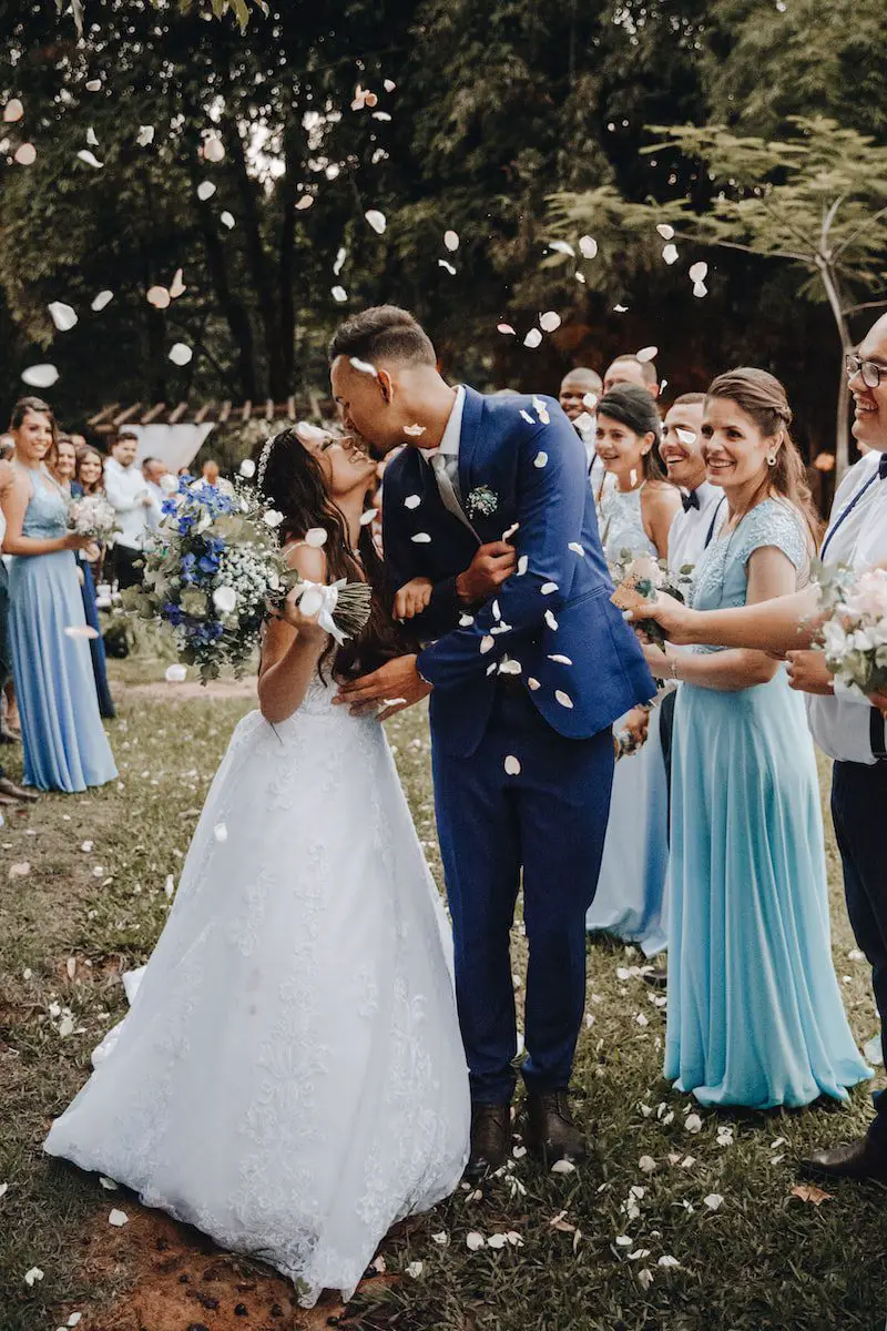 student in blue suit kissing woman in white wedding dress