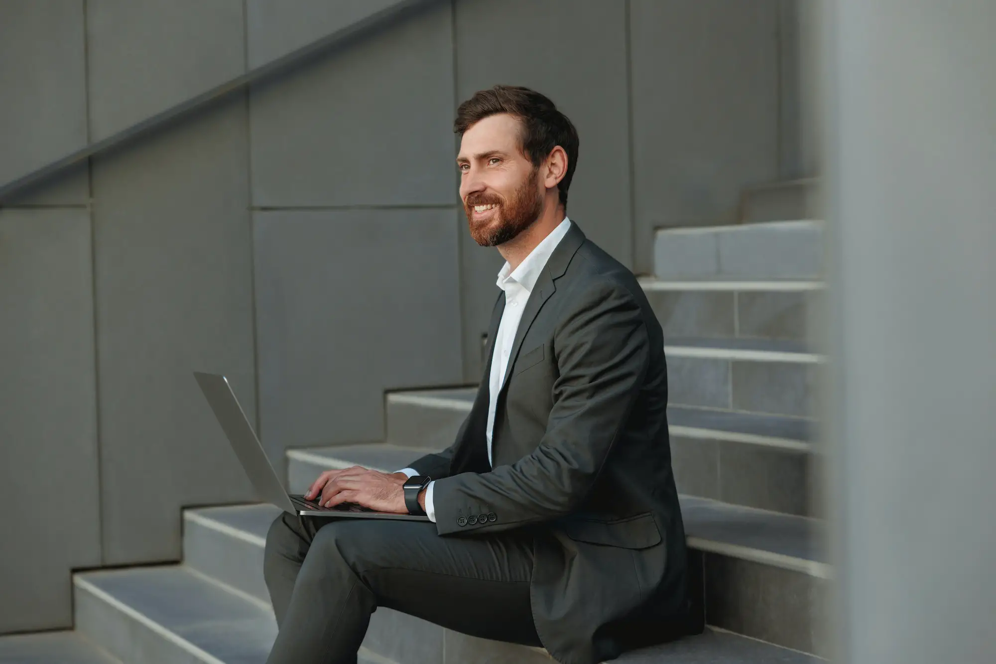 Focused Businessman working on laptop sitting on stairs outside office building