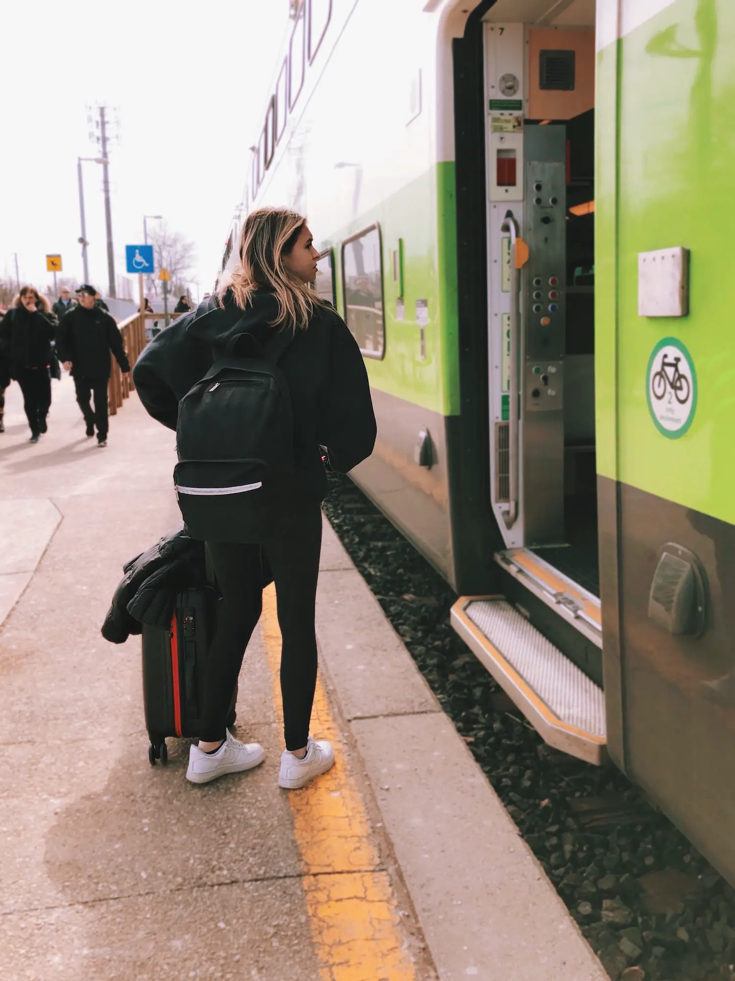 Young girl with a suitcase and backpack is getting on a train, public transportation