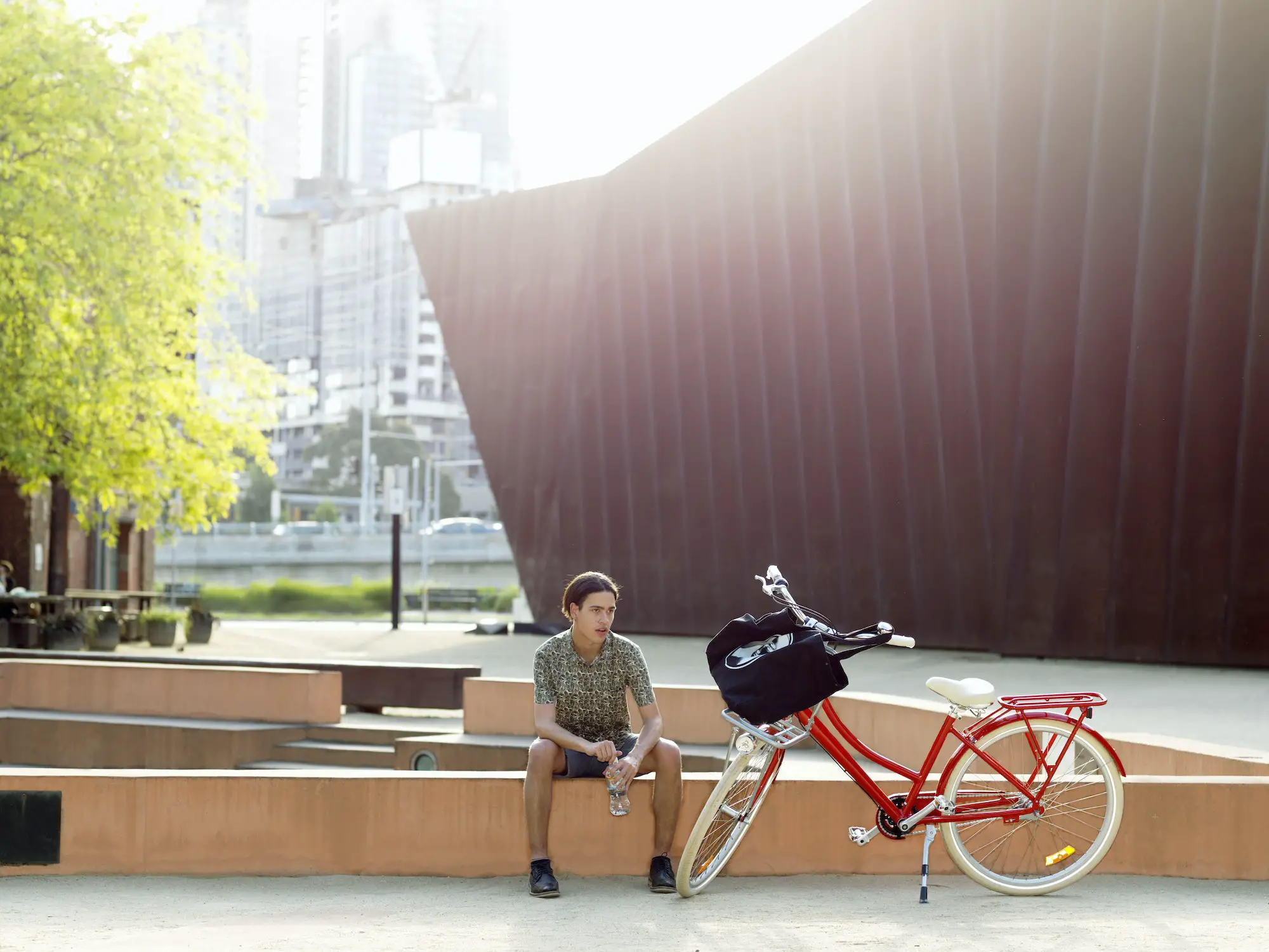 Young man taking break beside bicycle, Southbank, Melbourne, Australia